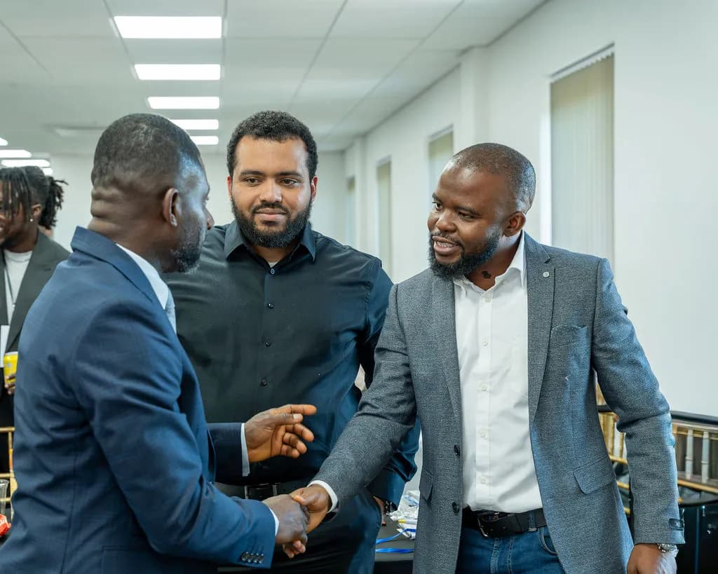 Two men shaking hands while a third looks on, networking in the hall