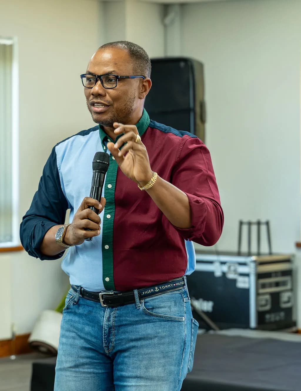 A speaker in a maroon and blue shirt gesturing as he talks into a microphone
