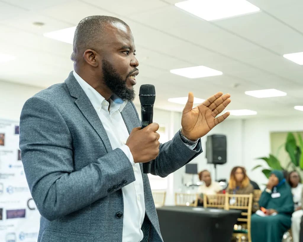 A speaker in a grey blazer making a point to the audience