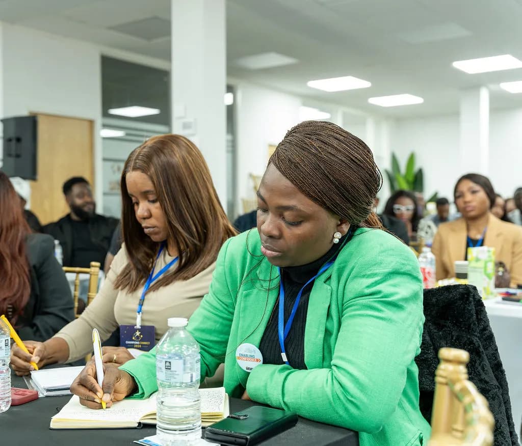 Two attendees taking notes by hand during a session