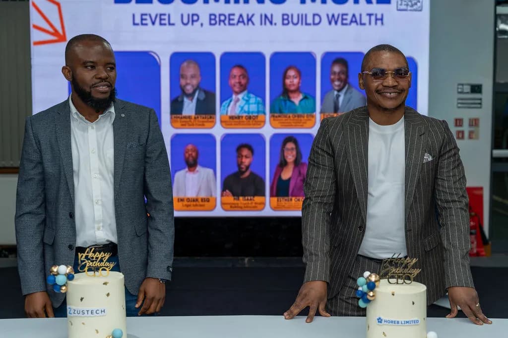 Two men standing behind celebration cakes in front of the stage screen