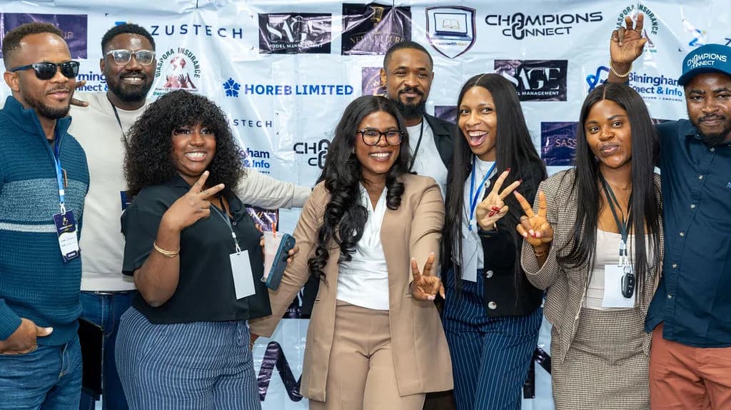 A group of attendees making peace signs and laughing in front of the sponsor backdrop