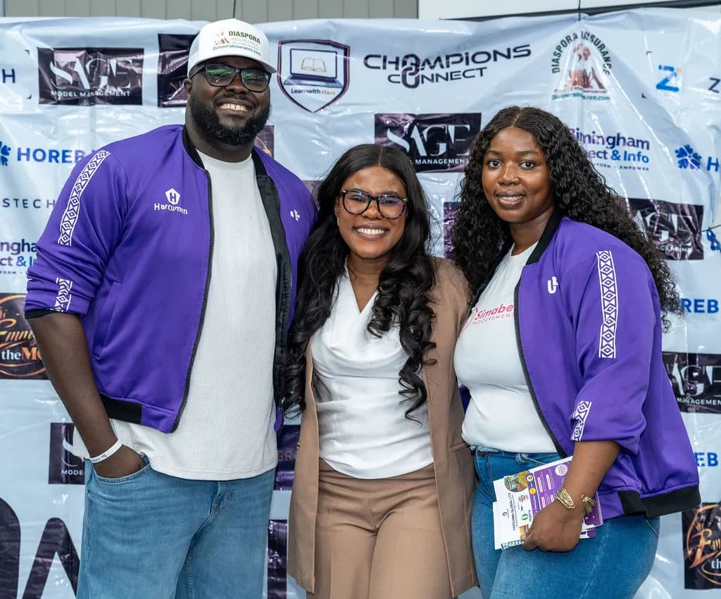 Three attendees smiling in front of the sponsor backdrop