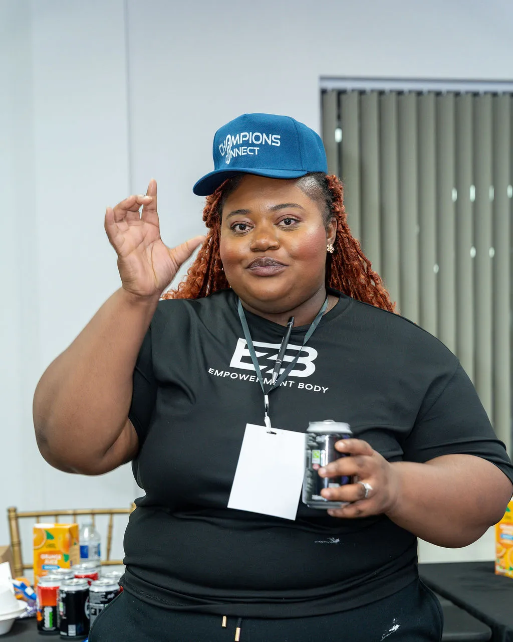 An attendee in a Champions Connect cap gesturing while holding a drink